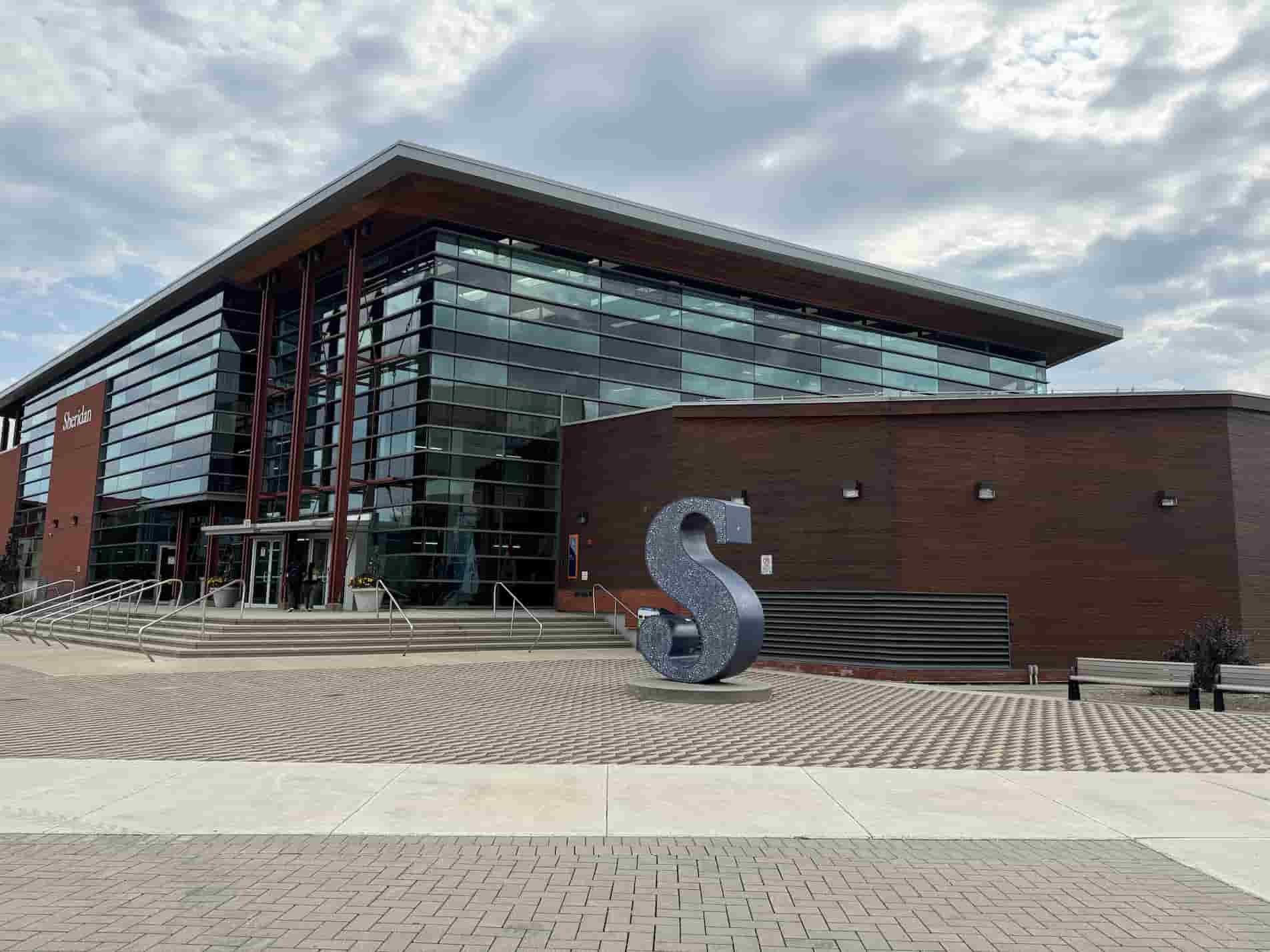 Spatial workshop 1 – Image of the exterior of the S-wing – The big blue “S” in front feels like a symbol of the school. It stands out clearly on the grey and white ground and in front of the dark red building. The building itself uses a lot of glass and windows, which makes the space feel bright and open, but still separate from the outside. I think this design shows a concept between openness and privacy, and how materials can make people feel connected to the space.